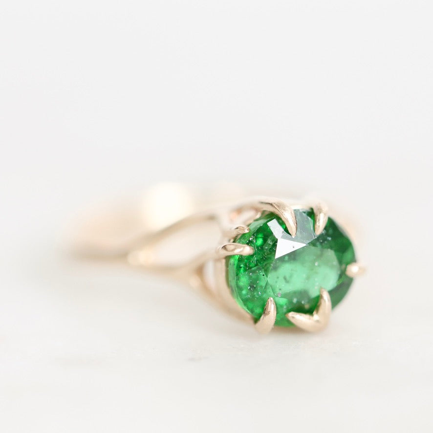 A round-cut green gemstone ring in a gold claw setting, photographed on a clean white background.