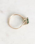 A gold ring with a split shank and a small green rectangular gemstone, photographed on a light marble surface.