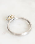 A silver ring with two small gold bezel-set clear stones, photographed on a light marble-like surface.