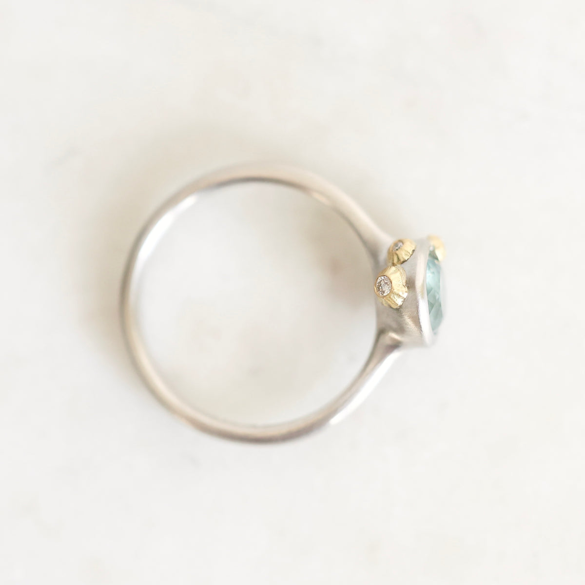 A silver ring with a small cluster of yellow gold stones and a light blue oval gemstone, photographed on a white marble surface.