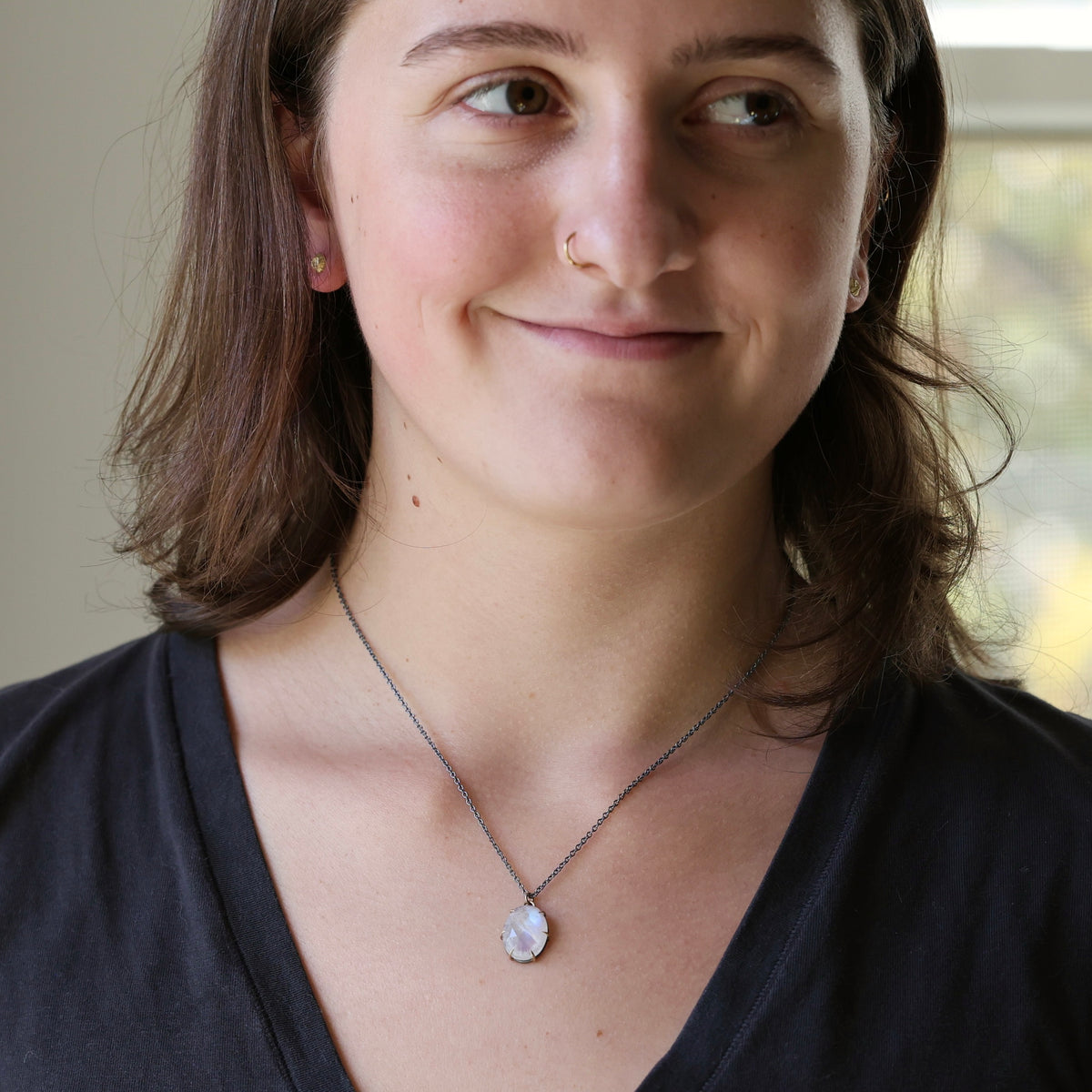 A woman wearing a silver chain necklace with a  white pendant, shown in a close-up portrait.