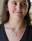 A woman wearing a silver chain necklace with a  white pendant, shown in a close-up portrait.