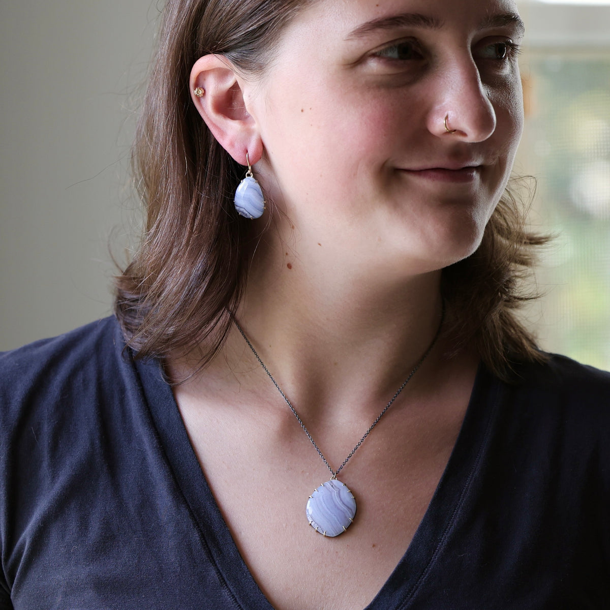 A woman wearing a matching jewelry set featuring a light blue-gray seashell pendant necklace and matching shell drop earrings on a silver chain.