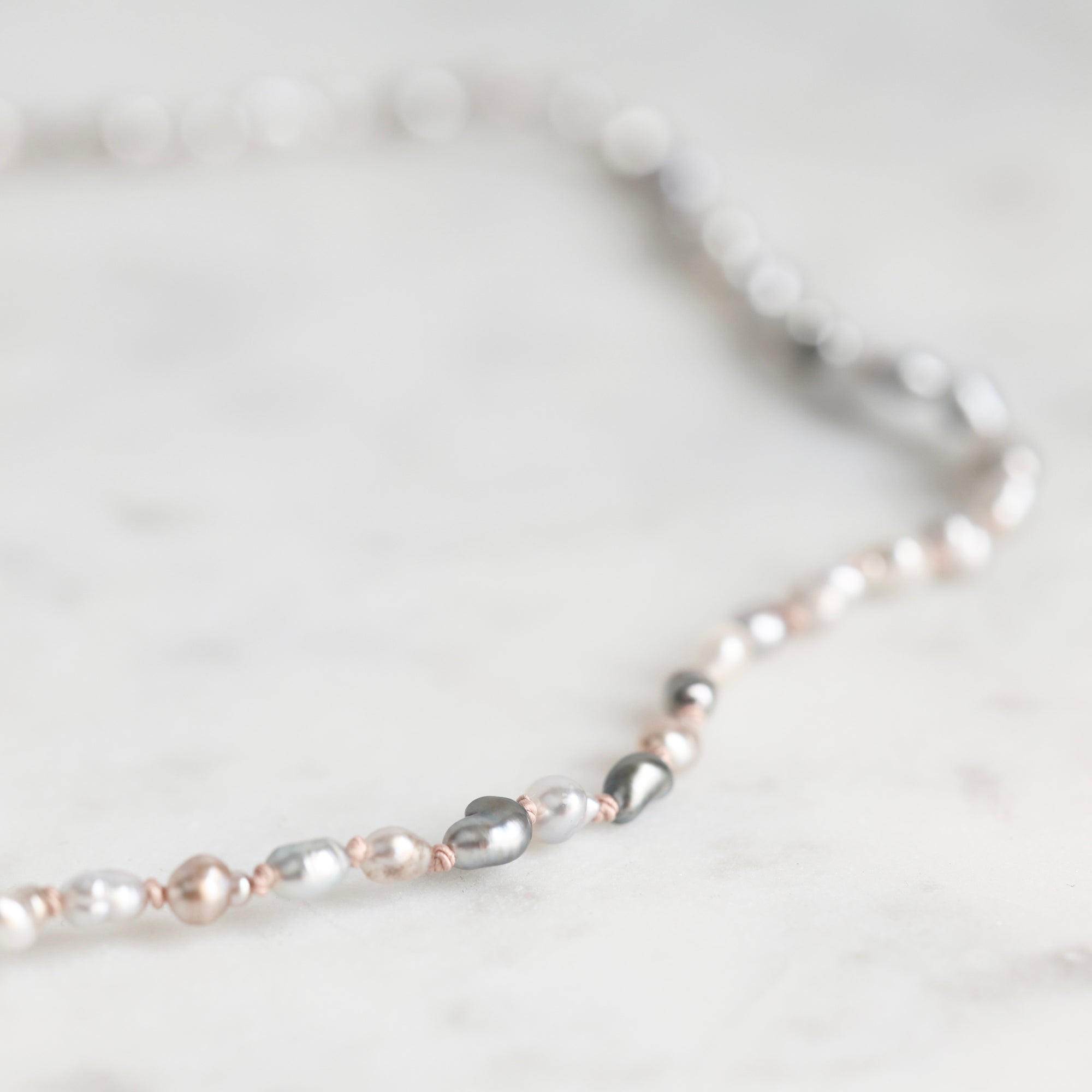 A delicate necklace featuring a mix of white, silver, and rose gold pearls threaded with small rose gold beads, displayed on a light marble surface.