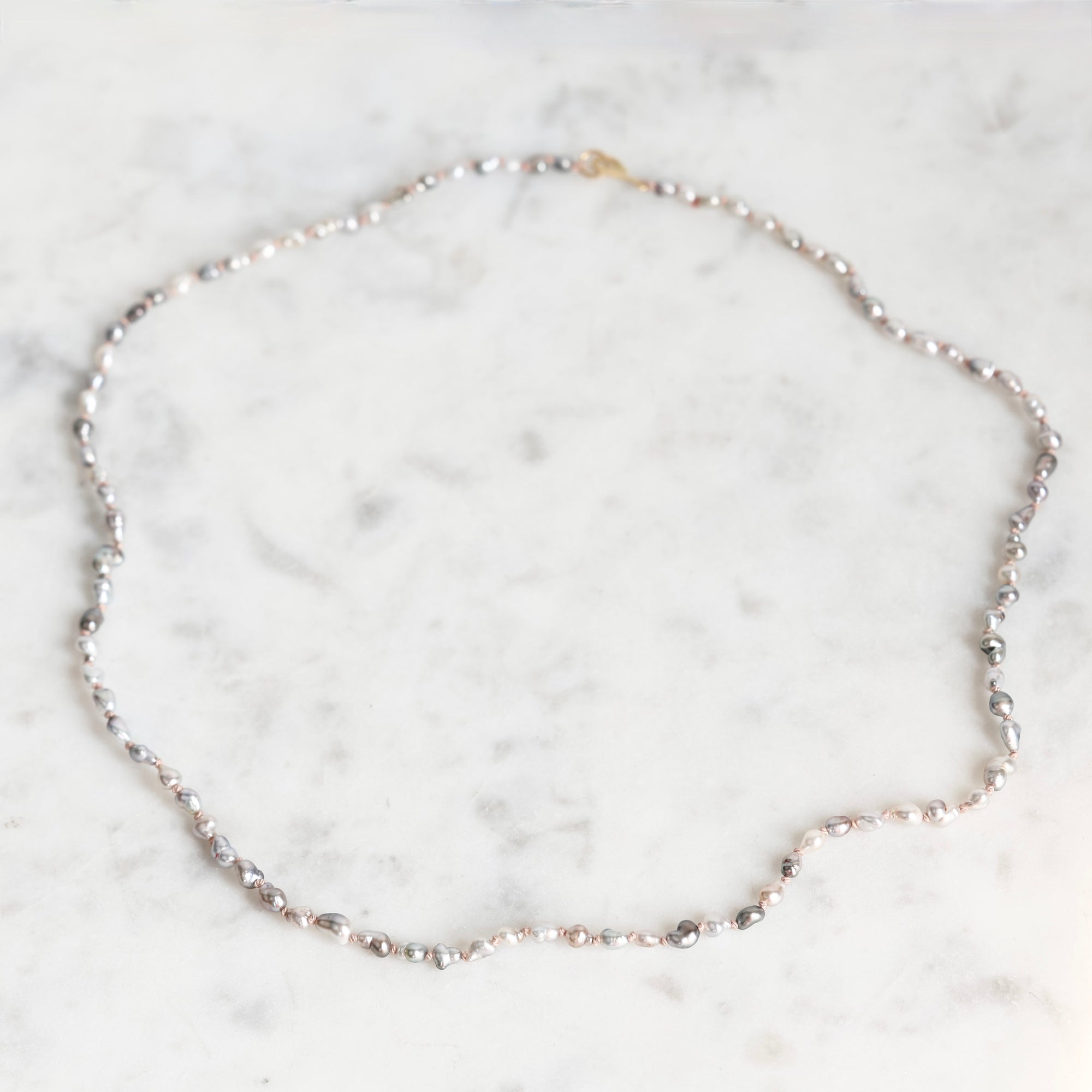 A delicate silver-toned beaded necklace with a small gold clasp, displayed on a white marble surface.
