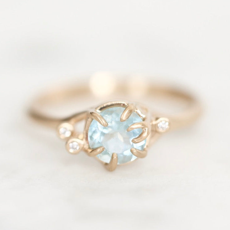 Light blue gemstone held in branchy gold prongs surrounded by diamond berries. 