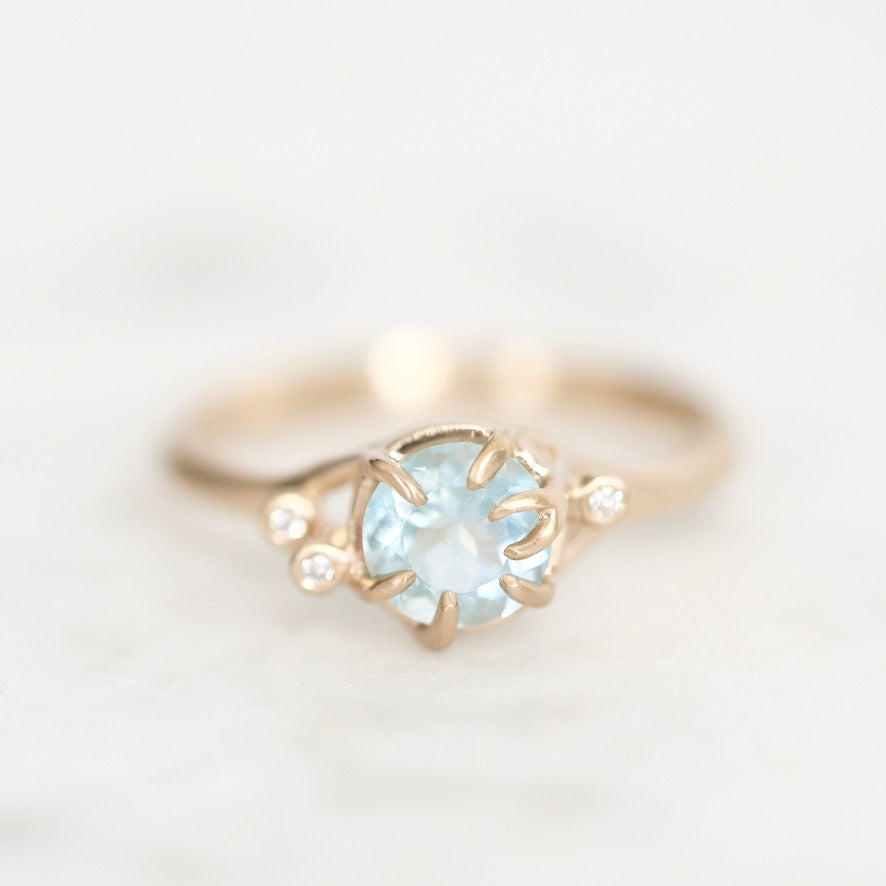 Light blue gemstone held in branchy gold prongs surrounded by diamond berries. 