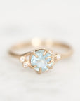 Light blue gemstone held in branchy gold prongs surrounded by diamond berries. 