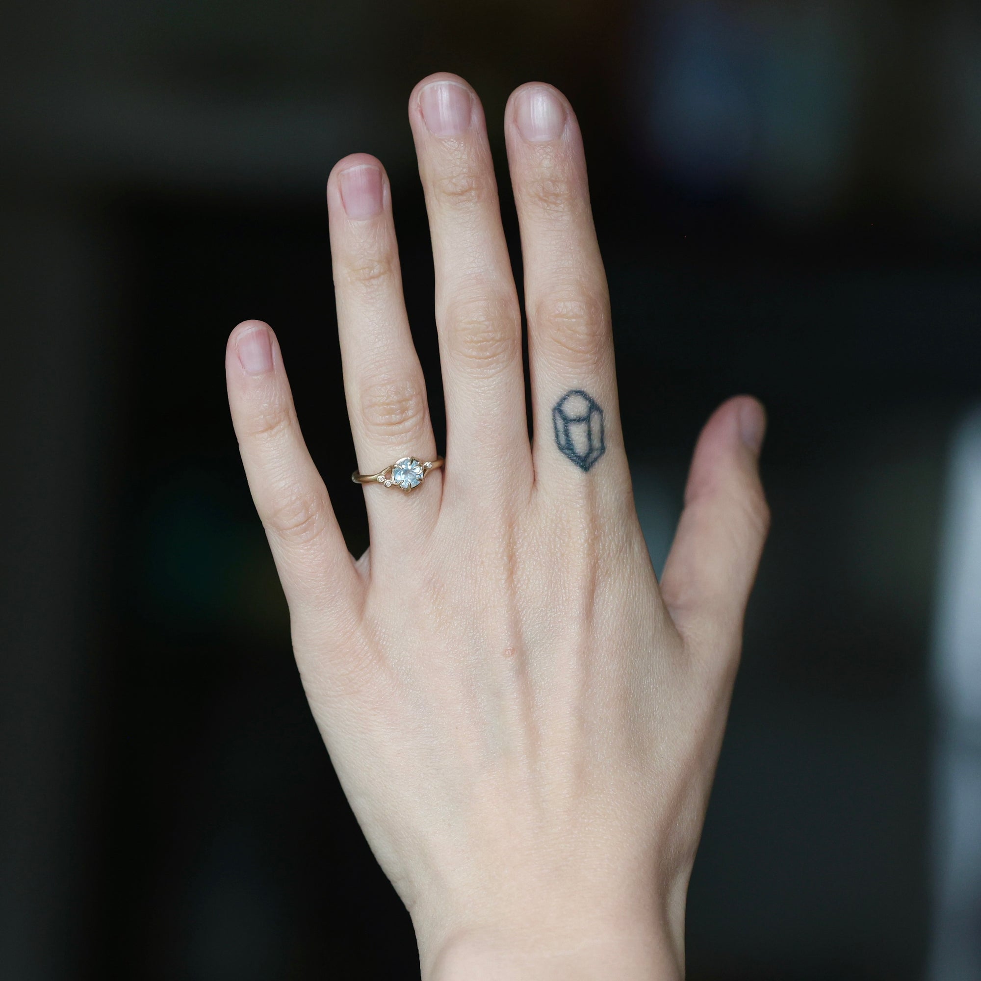 Blue stone ring on hand with tattoo. Center stone is surrounded by diamond berries. 