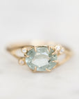 A yellow gold ring featuring a large oval-cut light blue gemstone in a prong setting, accented by two small round clear stones on the band, photographed on a soft white background.