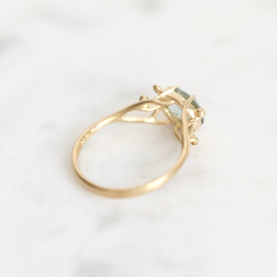 A gold ring with a small light blue-green gemstone, photographed on a white marble surface.