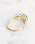 A gold ring with a small light blue-green gemstone, photographed on a white marble surface.