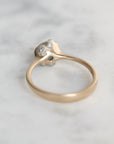 A vintage-style ring with a yellow gold band and a silver-toned setting featuring small clear gemstones, resting on a light gray marble surface.