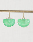 A pair of green shell-shaped drop earrings with gold hooks, hanging from a gold-colored horizontal bar against a light gray background.