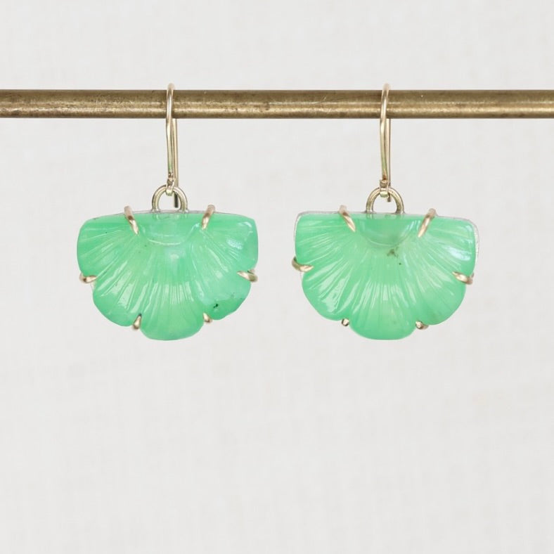 A pair of green shell-shaped drop earrings with gold hooks, hanging from a gold-colored horizontal bar against a light gray background.
