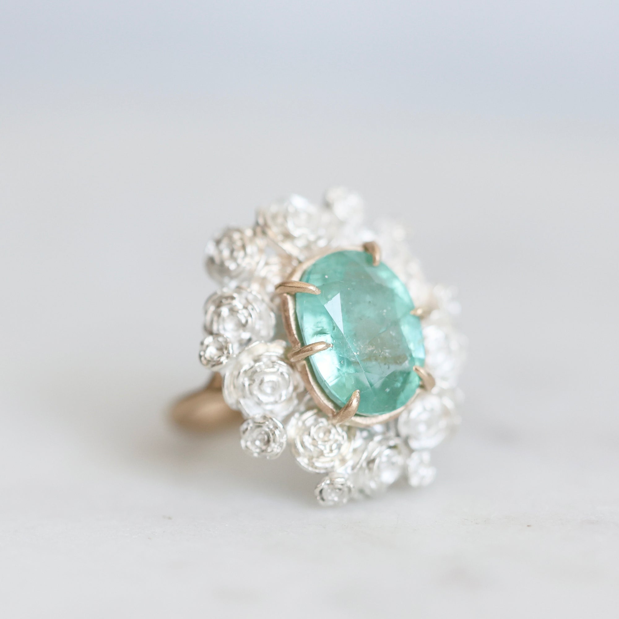 Glowing green stone held in gold prongs surrounded by silver roses 