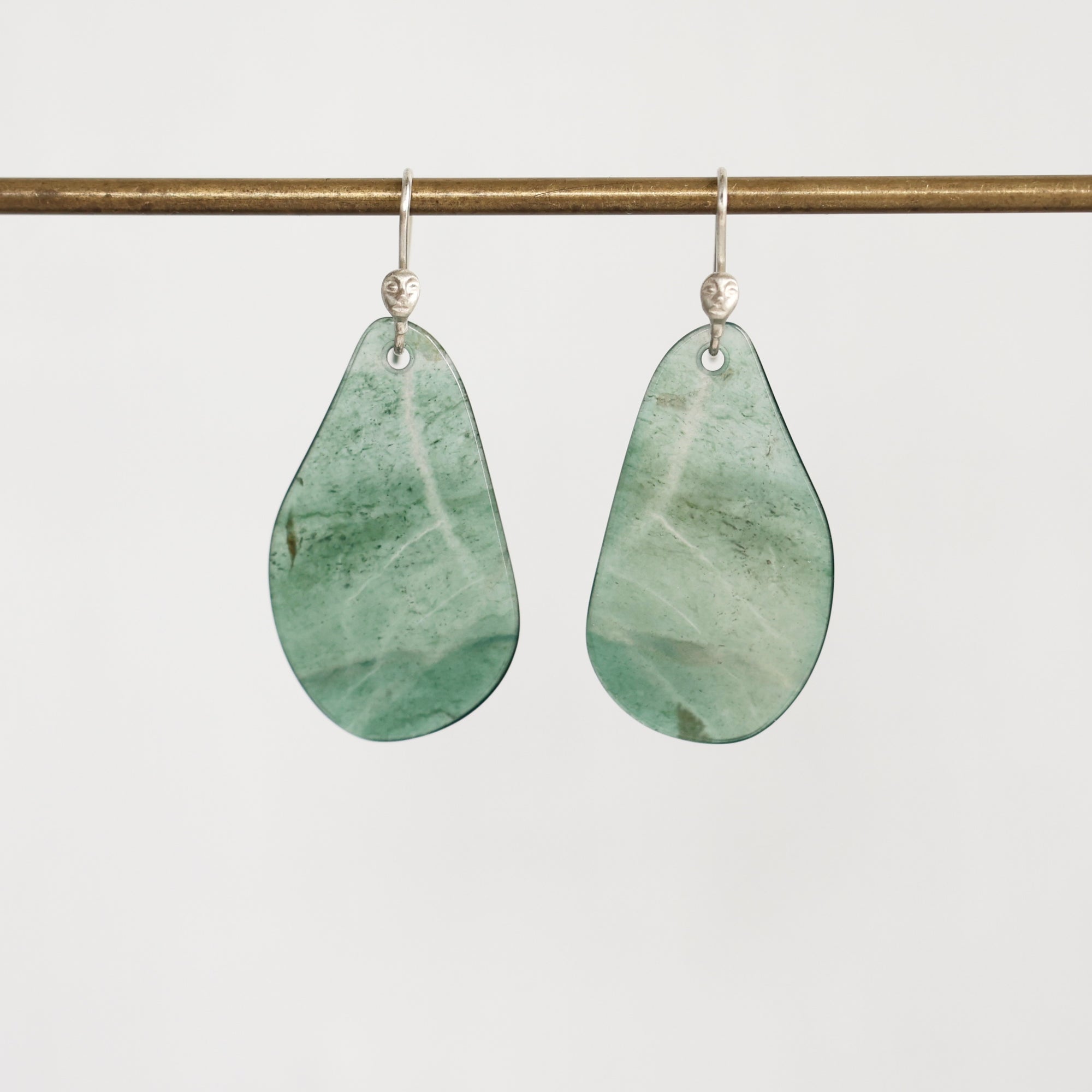 A pair of teardrop-shaped drop earrings made from light green marbled stone, hanging from silver fishhook wires against a plain light gray background.