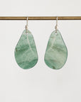 A pair of teardrop-shaped drop earrings made from light green marbled stone, hanging from silver fishhook wires against a plain light gray background.
