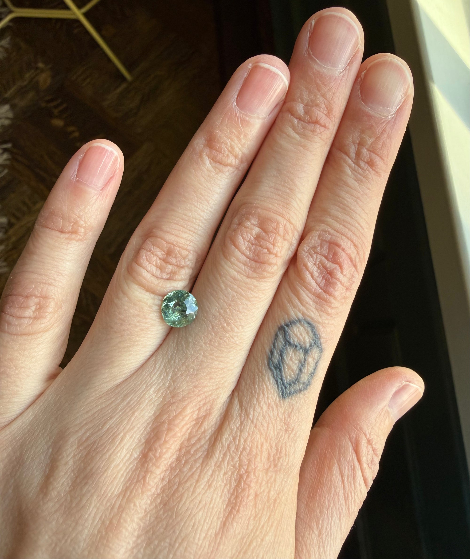 Hand with a green gemstone ring on a finger, with a small tattoo 