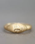 A gold ring sculpted in the shape of a stylized face, photographed against a neutral gray background.