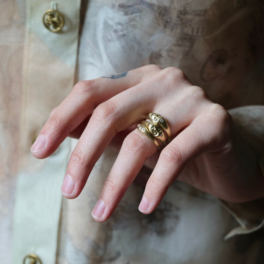 A close-up of a hand wearing three stacked gold rings, with a soft-focus background showing a patterned garment.