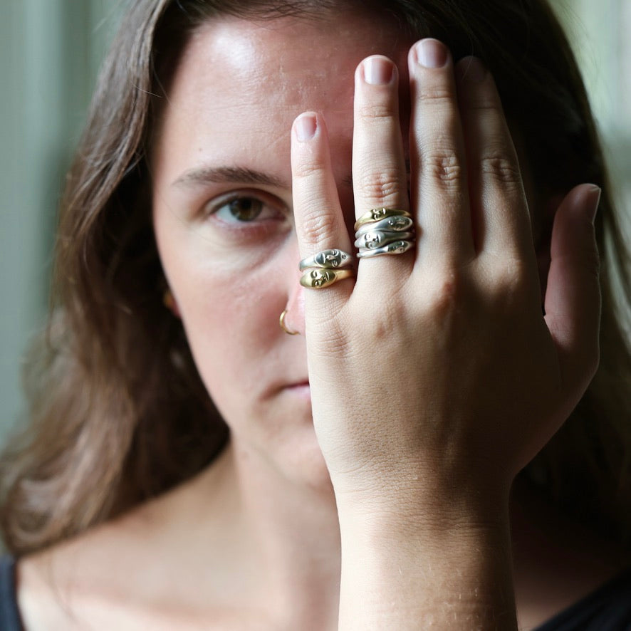 A close-up lifestyle shot of a woman wearing three stacked rings on her finger. The rings feature organic, snake-like textured bands in gold and silver metals.
