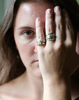 A close-up lifestyle shot of a woman wearing three stacked rings on her finger. The rings feature organic, snake-like textured bands in gold and silver metals.