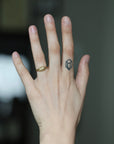 A close-up of a person's hand with a small geometric tattoo on the ring finger and a gold ring on the middle finger, set against a blurred dark background.