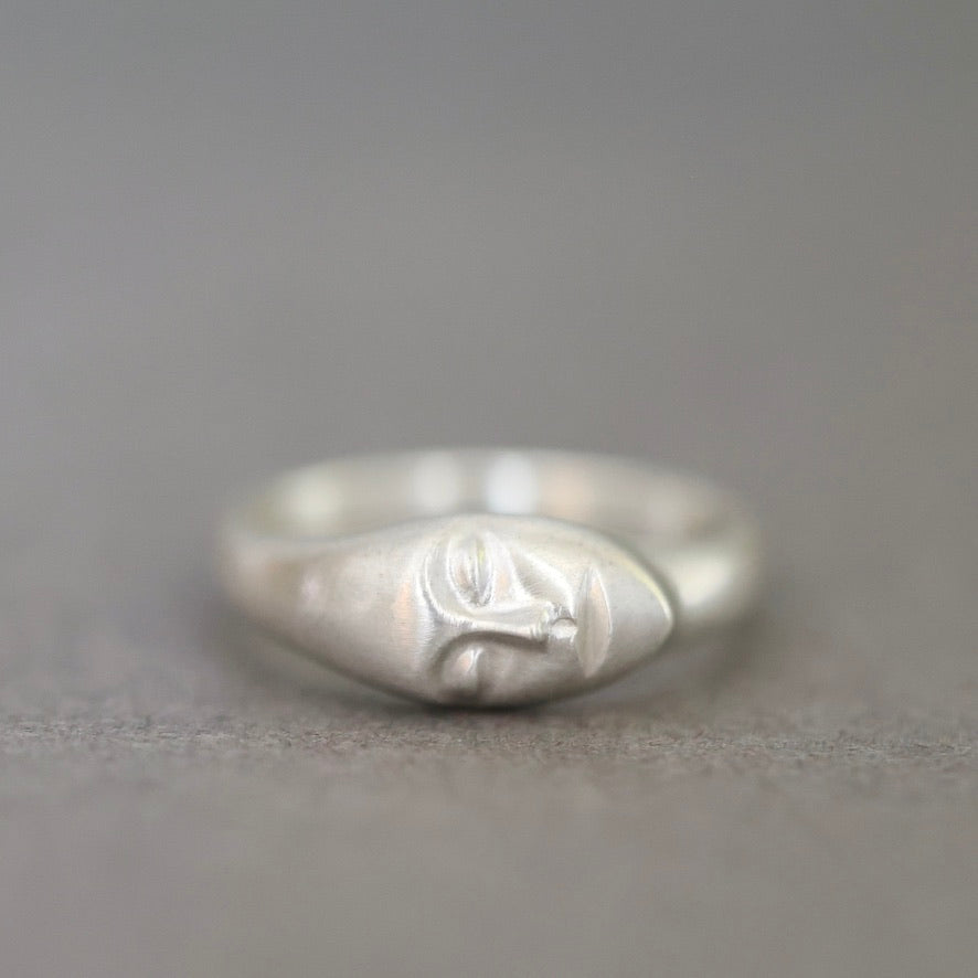 A sterling silver ring featuring a stylized, abstract sculpted face on the band, photographed against a neutral gray background.