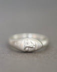 A sterling silver ring featuring a stylized, abstract sculpted face on the band, photographed against a neutral gray background.