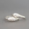 A pair of silver rings shaped like stylized faces, with one ring featuring a small clear gemstone, set against a soft gray background.