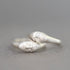 A pair of silver rings shaped like stylized faces, with one ring featuring a small clear gemstone, set against a soft gray background.
