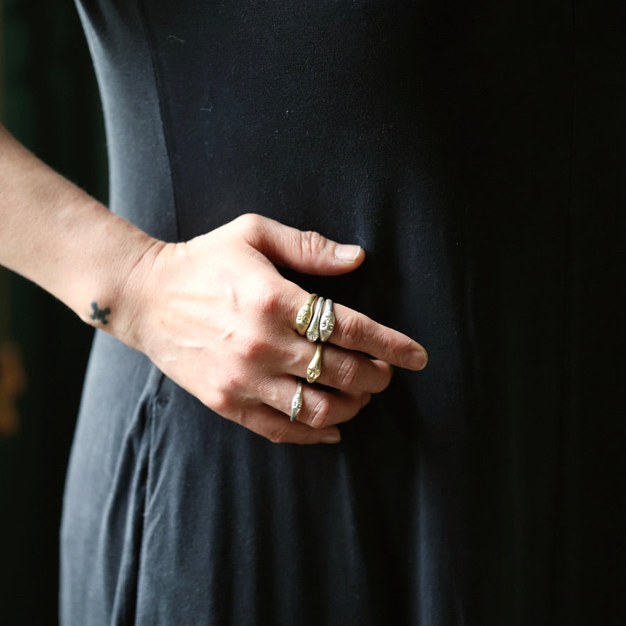 A close-up of a person's hand wearing multiple gold rings, including one with a marquise-cut gemstone and others with textured bands, set against a dark black dress.