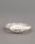 A sterling silver ring shaped like a stylized face with a small clear gemstone, photographed on a neutral gray background.
