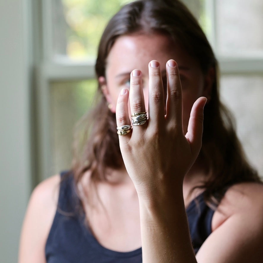 A woman wearing multiple stacked silver rings on one finger, holding her hand up in front of her face in a softly lit indoor setting.