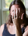 A woman wearing multiple stacked silver rings on one finger, holding her hand up in front of her face in a softly lit indoor setting.