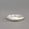 A sterling silver ring featuring a sculpted face with closed eyes and a small round clear gemstone on its cheek, set against a neutral gray background.