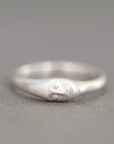 A sterling silver ring featuring a stylized, minimalist face carved into the band, set against a soft, neutral gray background.