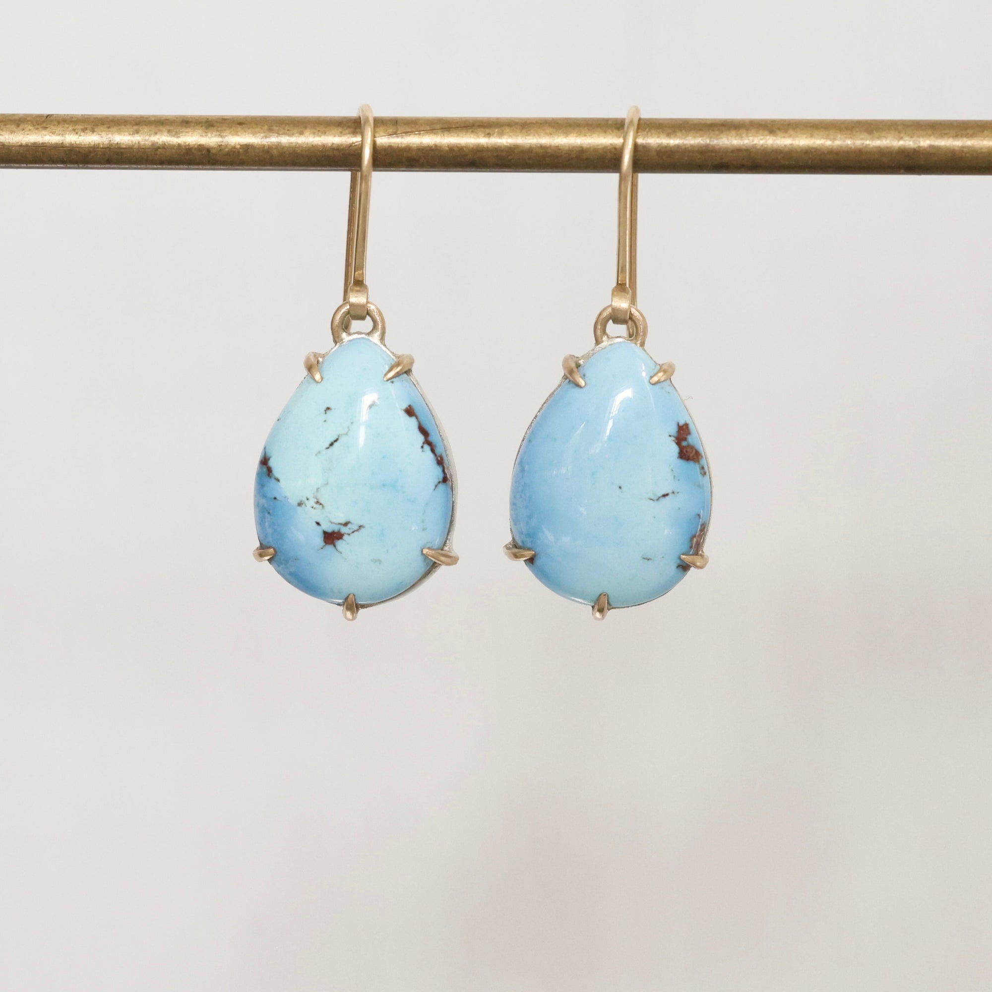 Pair of turquoise teardrop earrings on a gold hook against a light gray background