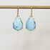Pair of turquoise teardrop earrings on a gold hook against a light gray background