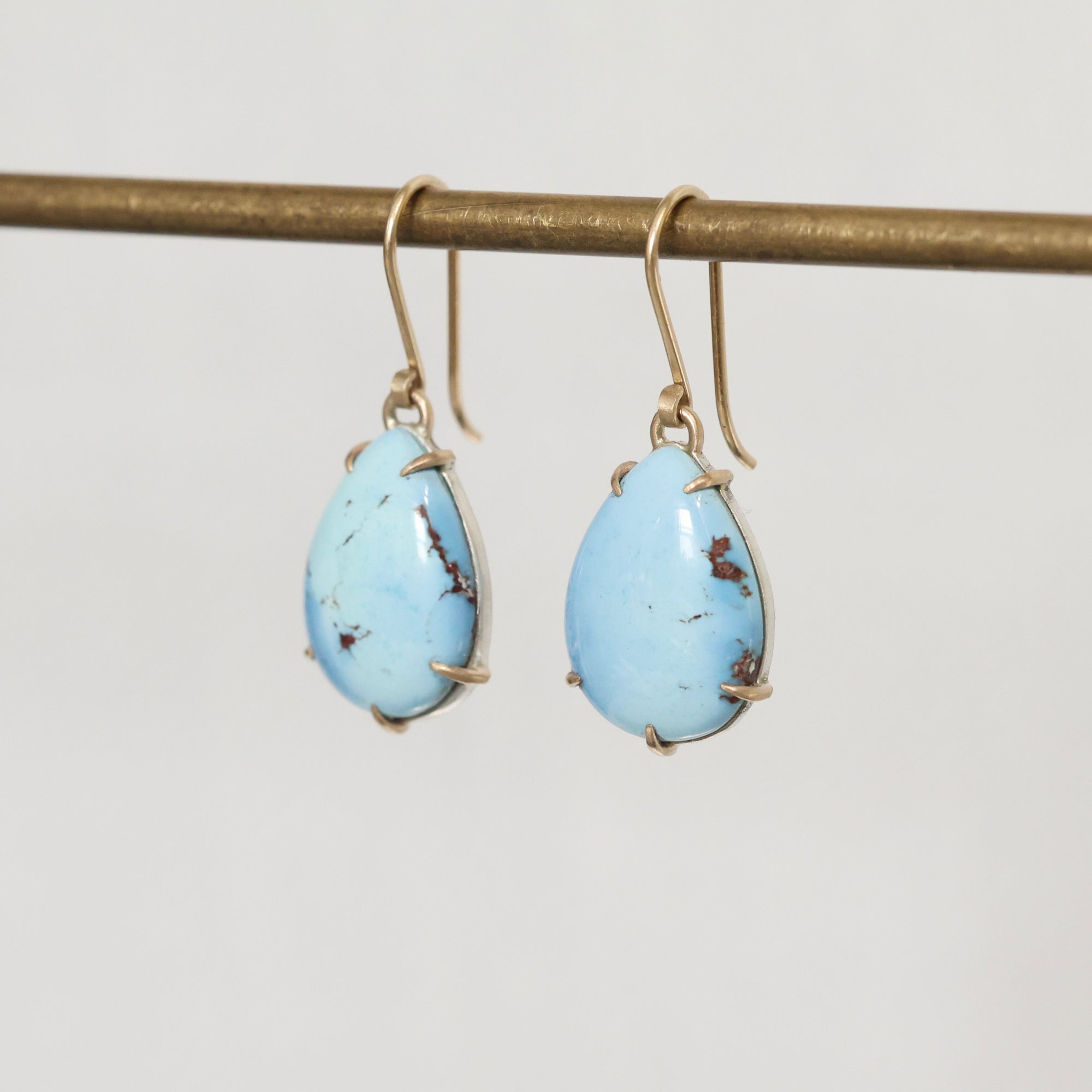 Turquoise teardrop earrings on a gold hook against a light gray background