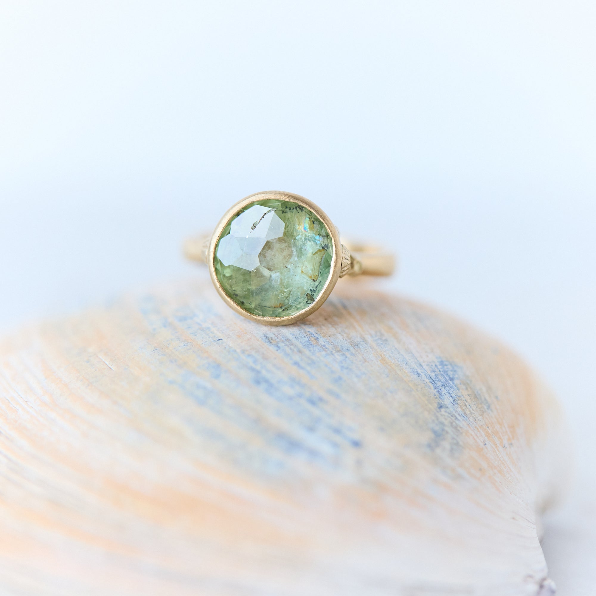 Gold ring with a green gemstone on a shell against a light background