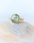 Gold ring with a green gemstone on a shell against a light background