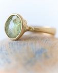 Gold ring with a green gemstone on a marble surface