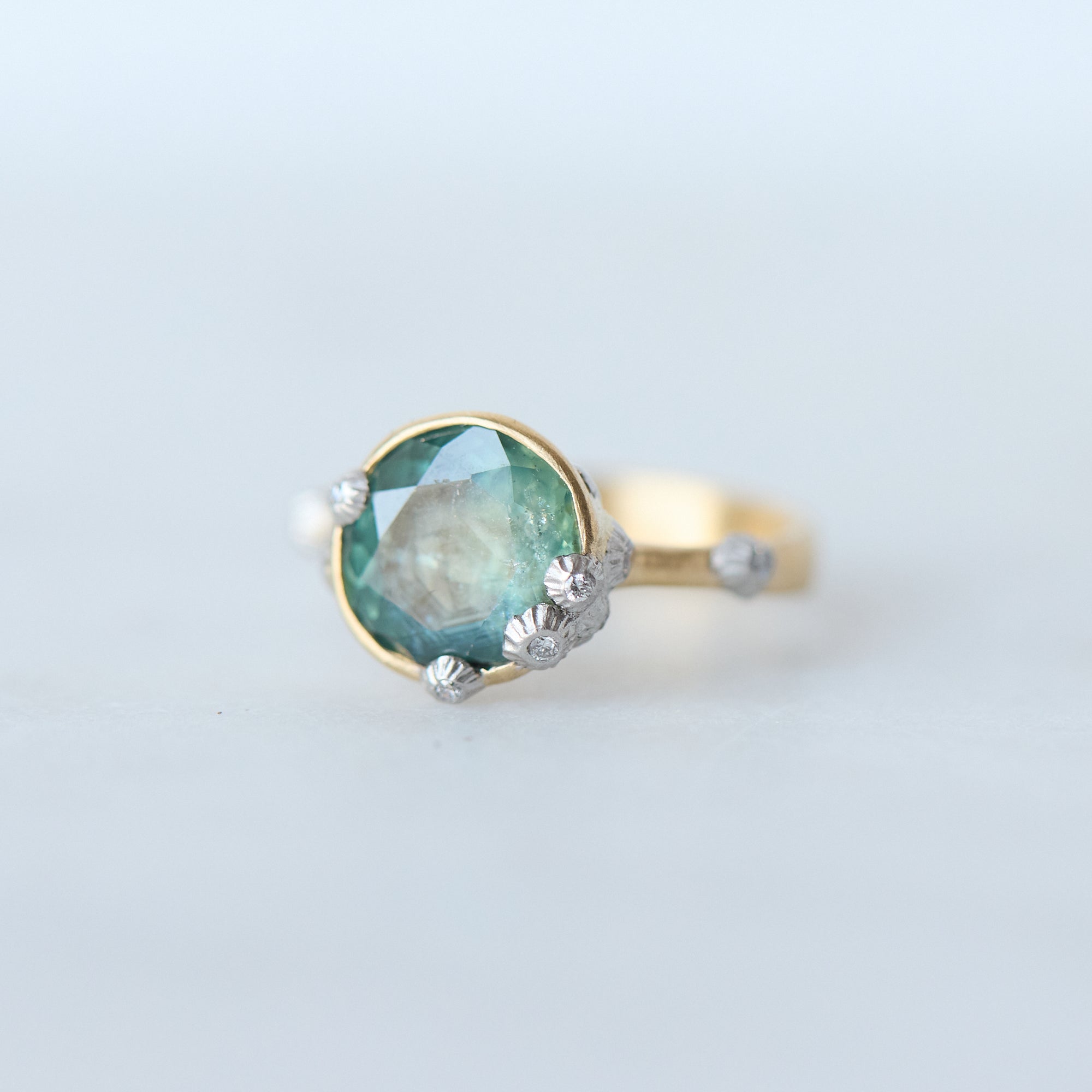 Gold ring with a green gemstone on a light gray background
