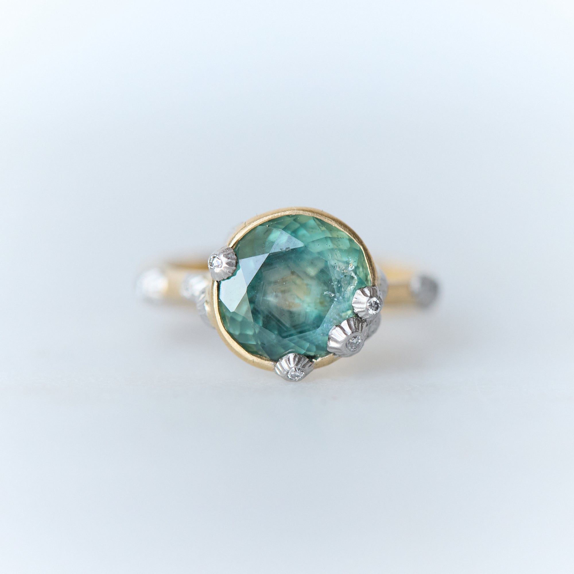 Ring with a green gemstone and gold band on a light gray background
