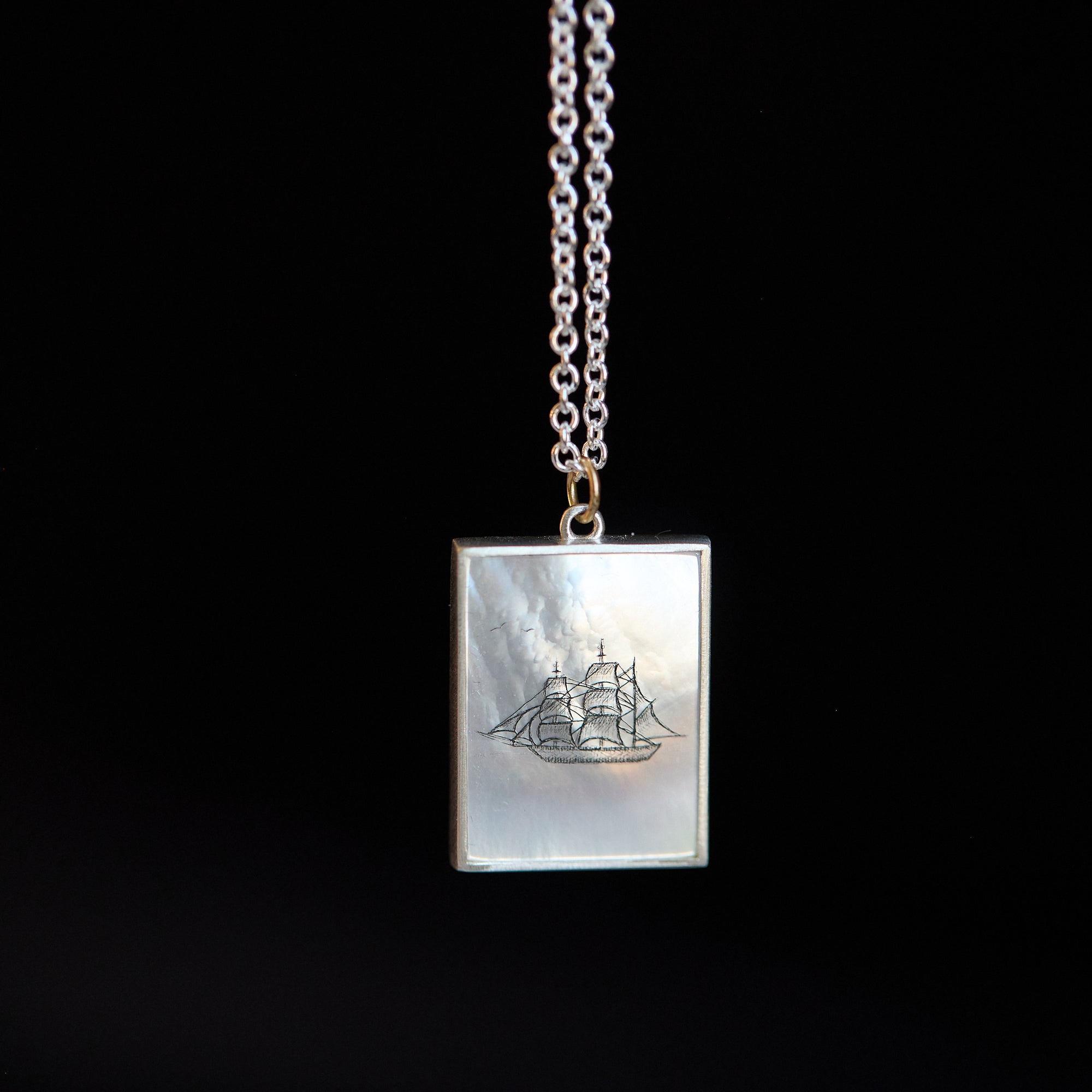 Necklace with a pendant featuring a ship design on a black background