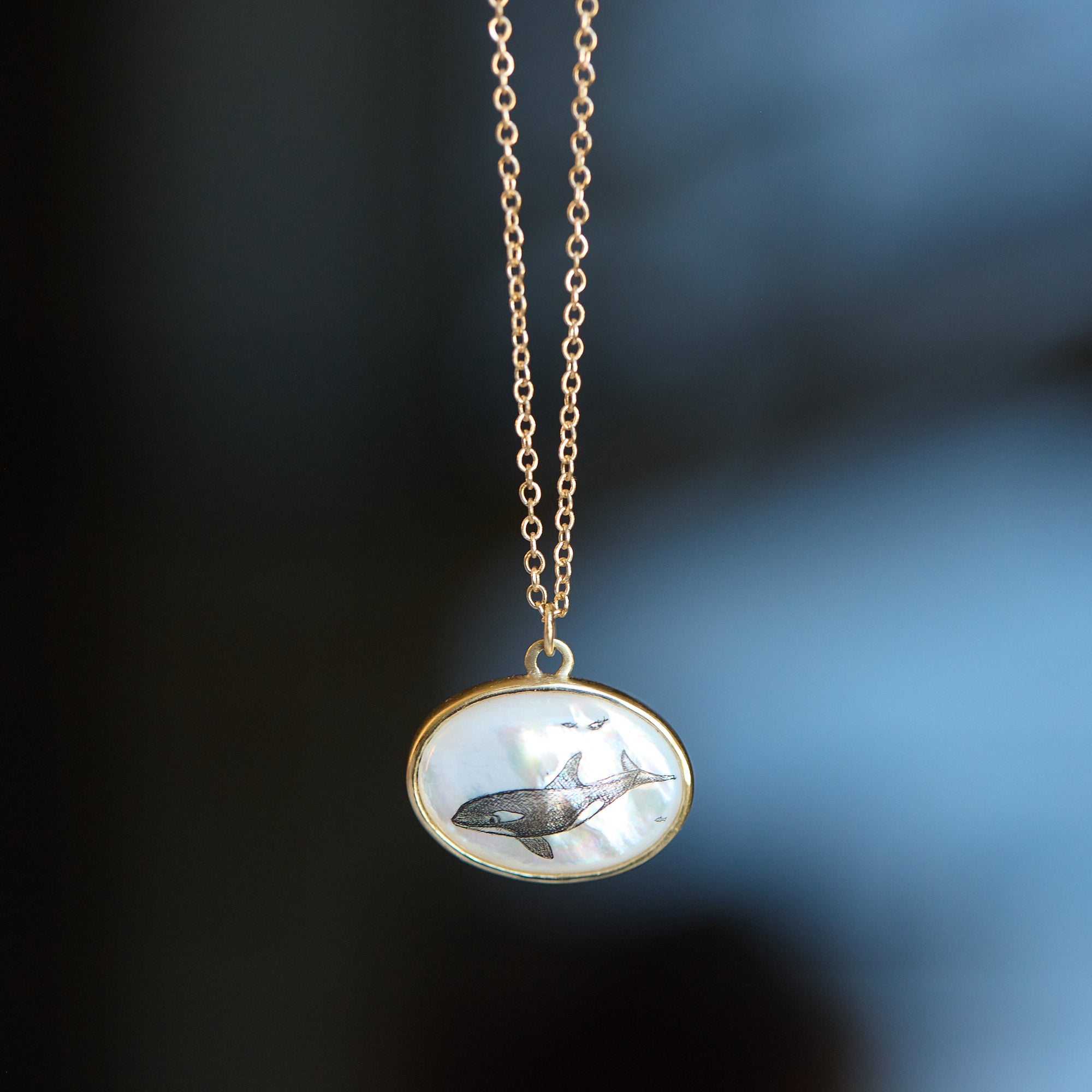 Gold necklace with a pendant featuring a whale design on a blurred background