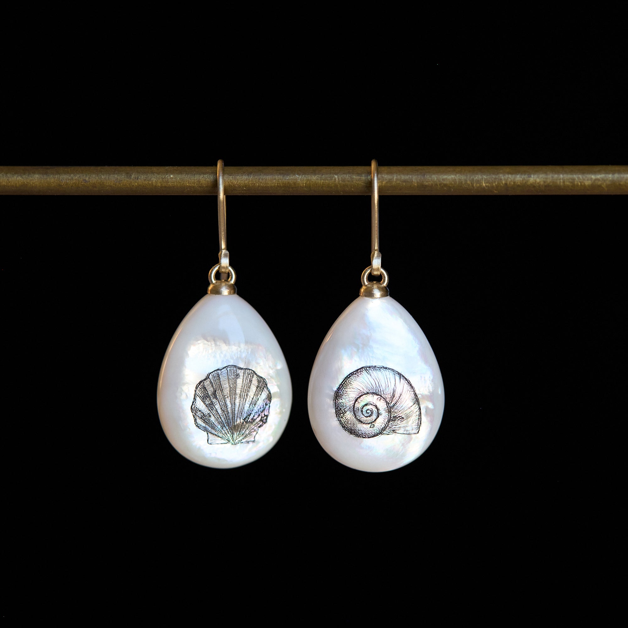 Pair of teardrop-shaped earrings with shell designs on a black background