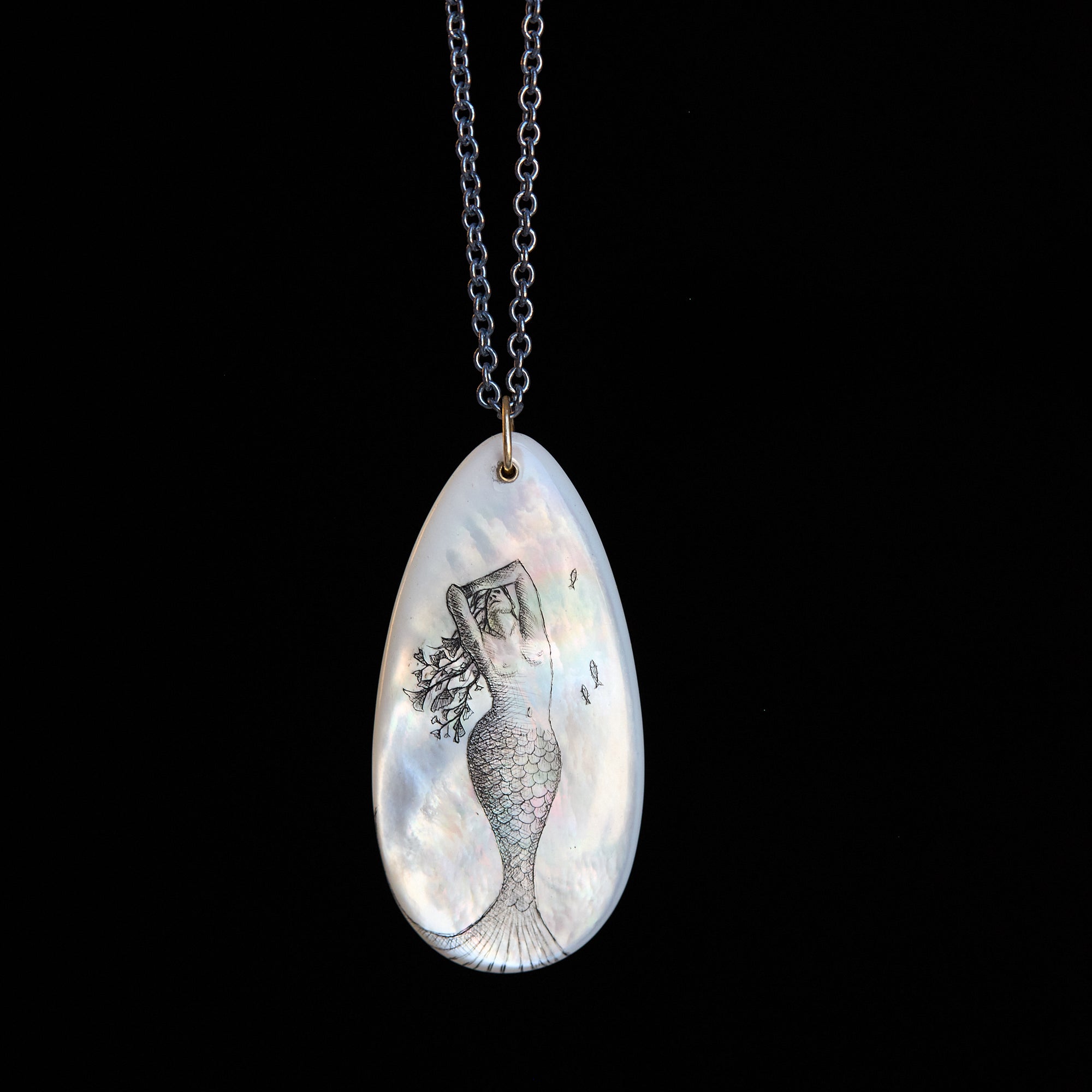 Teardrop-shaped pendant with mermaid design on a black background